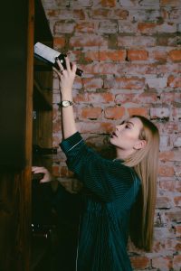 Elegant woman organizing bottles in a vintage cellar with a rustic brick wall background.